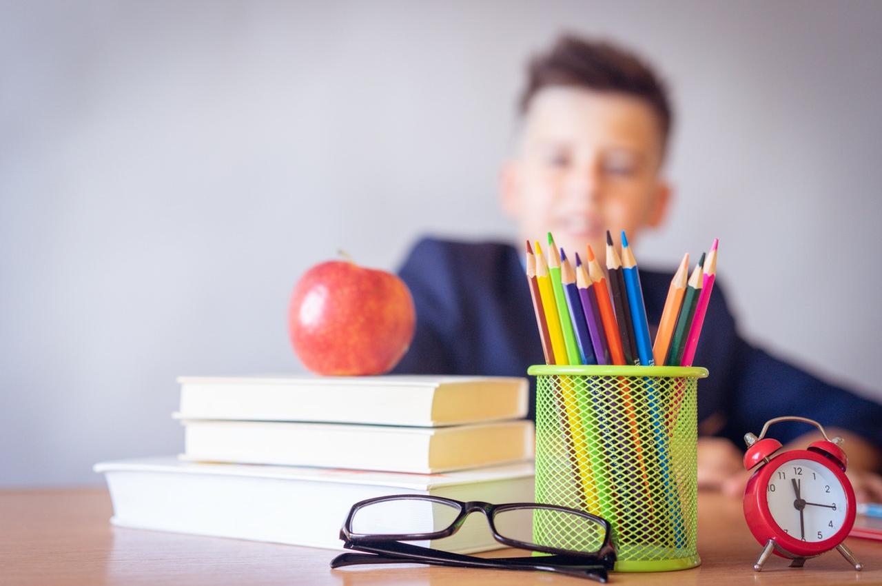boy looking at a book, apple and colored pencils on desk